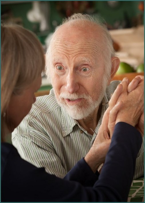 Senior couple at home in kitchen holding hands focusing on man